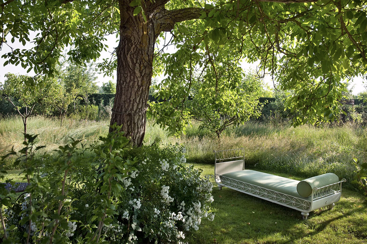 A sage green and white iron day bed beneath a tree at Borgo Santo Pietro