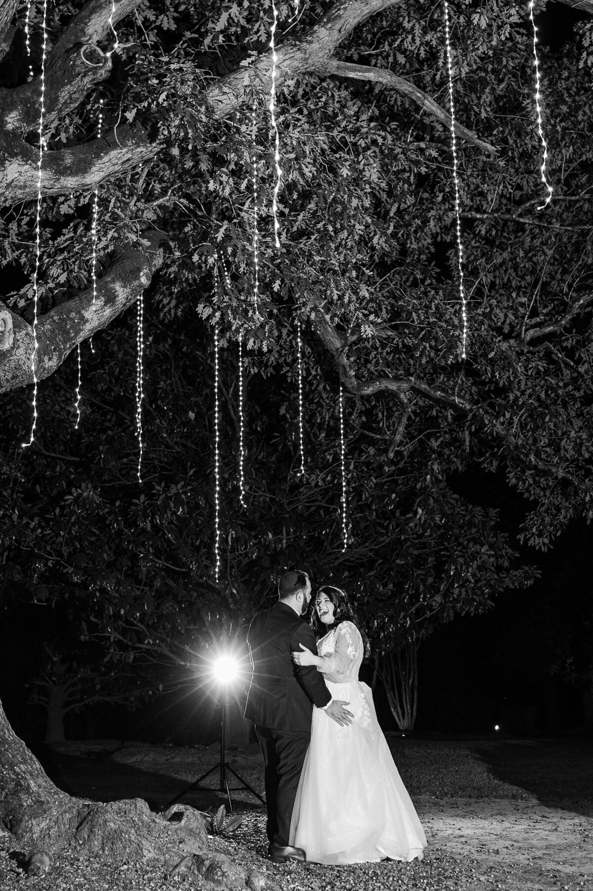 A bride and groom dancing and laughing under an oak tree with lights during their wedding reception by Raleigh wedding photographer. JoLynn Photography