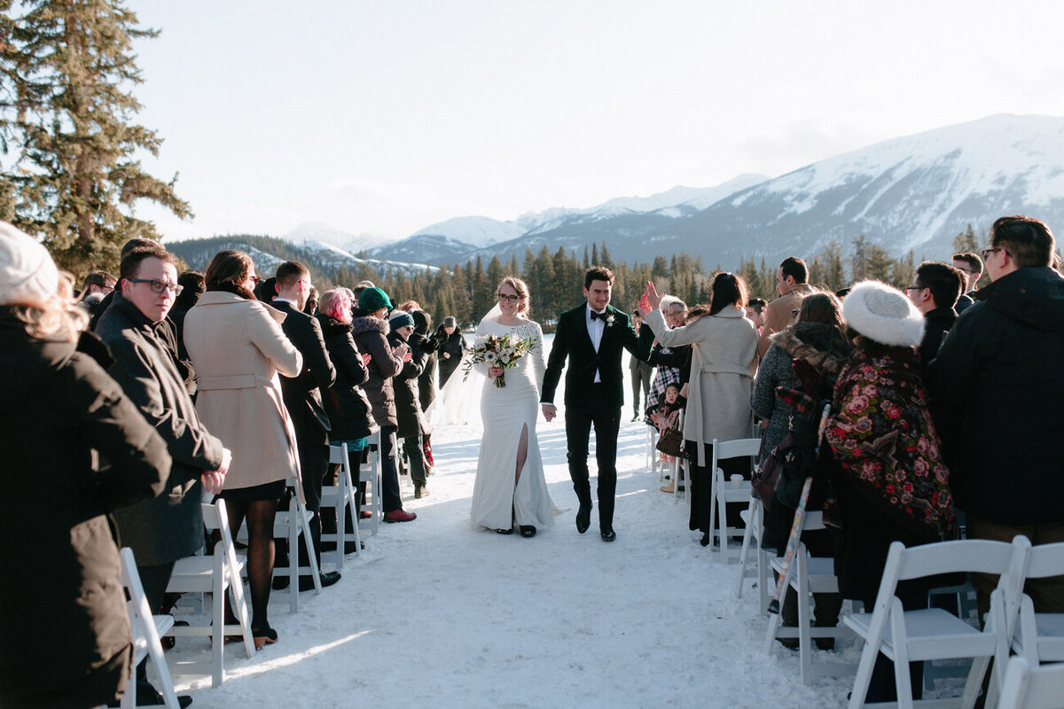 Bride and groom walking the aisle at their winter wedding with mountain landscape.
