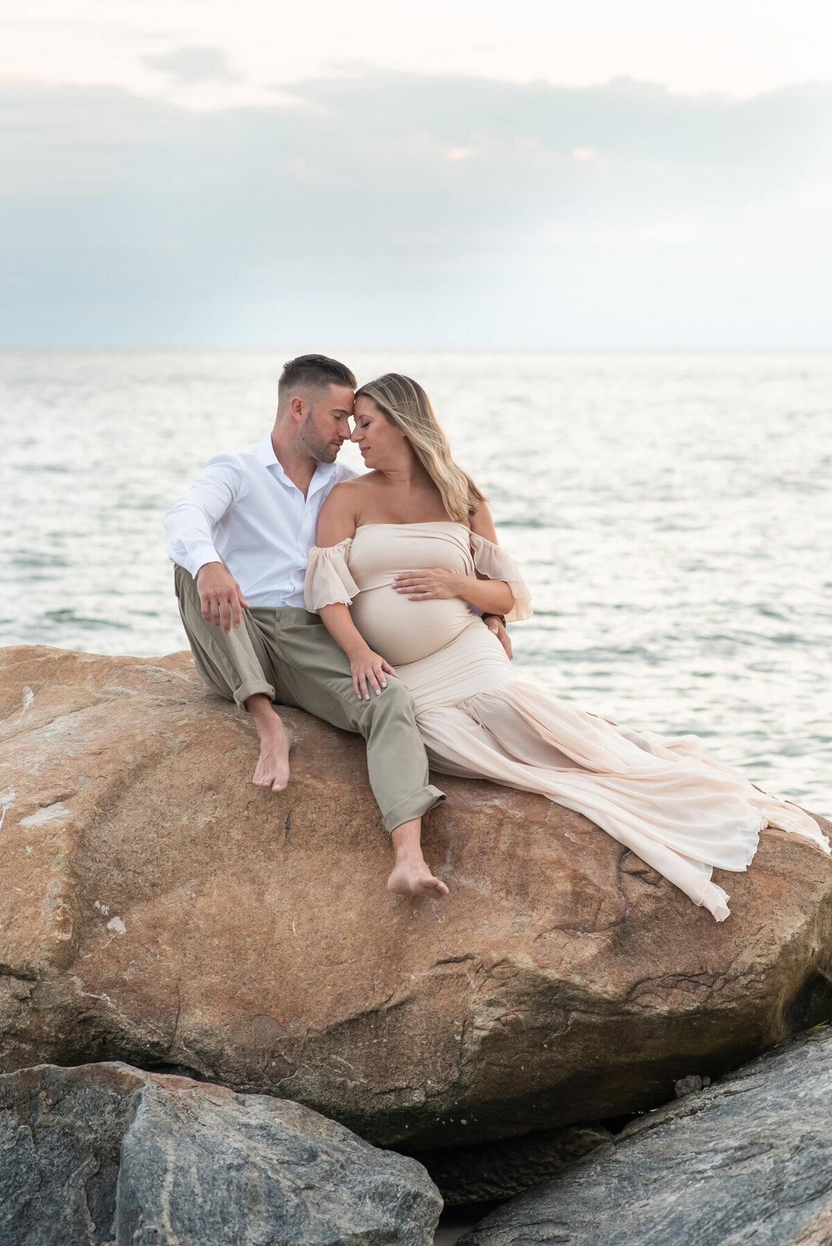 Couple on rock at sunset in maternity gown