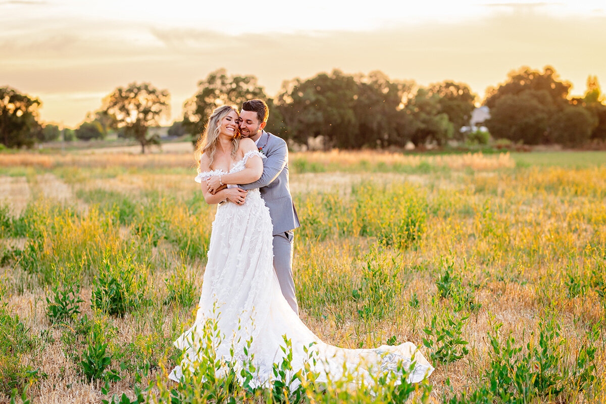Bride and groom cuddling in the fields at Le Reve Estate Lamoure Vineyards at sunset by Sacramento wedding photographer Ashley Teasley
