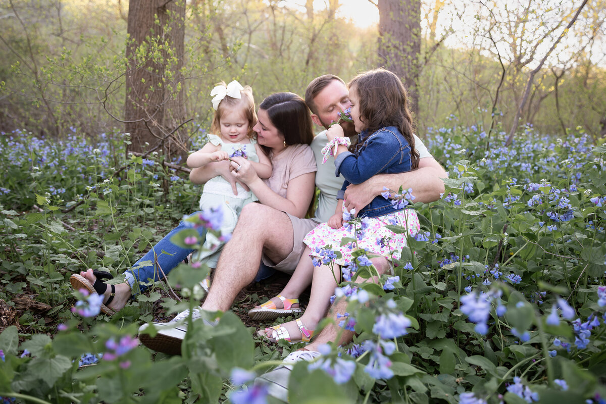 Parents cuddle and sniff bluebells during family photoshoot at Susquehanna State Park in Maryland