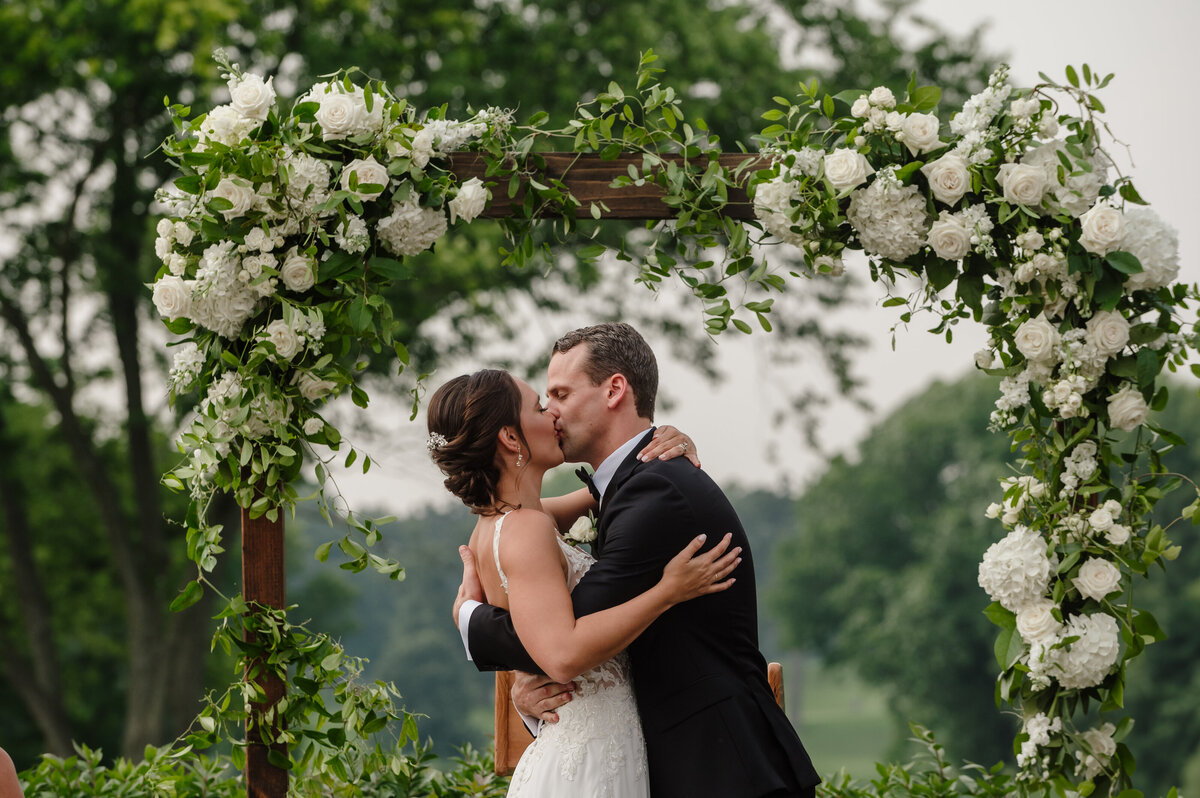 Bride and groom share first kiss in front of flower arch