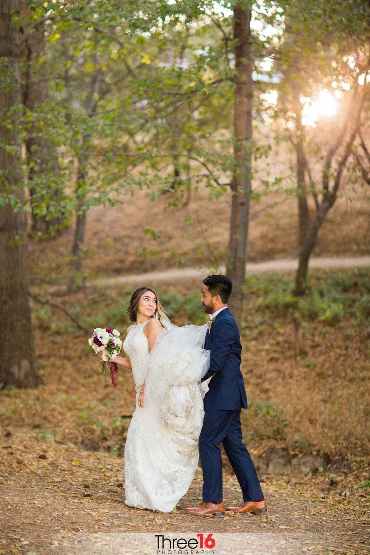 Bride looks back at her Groom as he carries her wedding dress train off the dirt during their walk in the woods