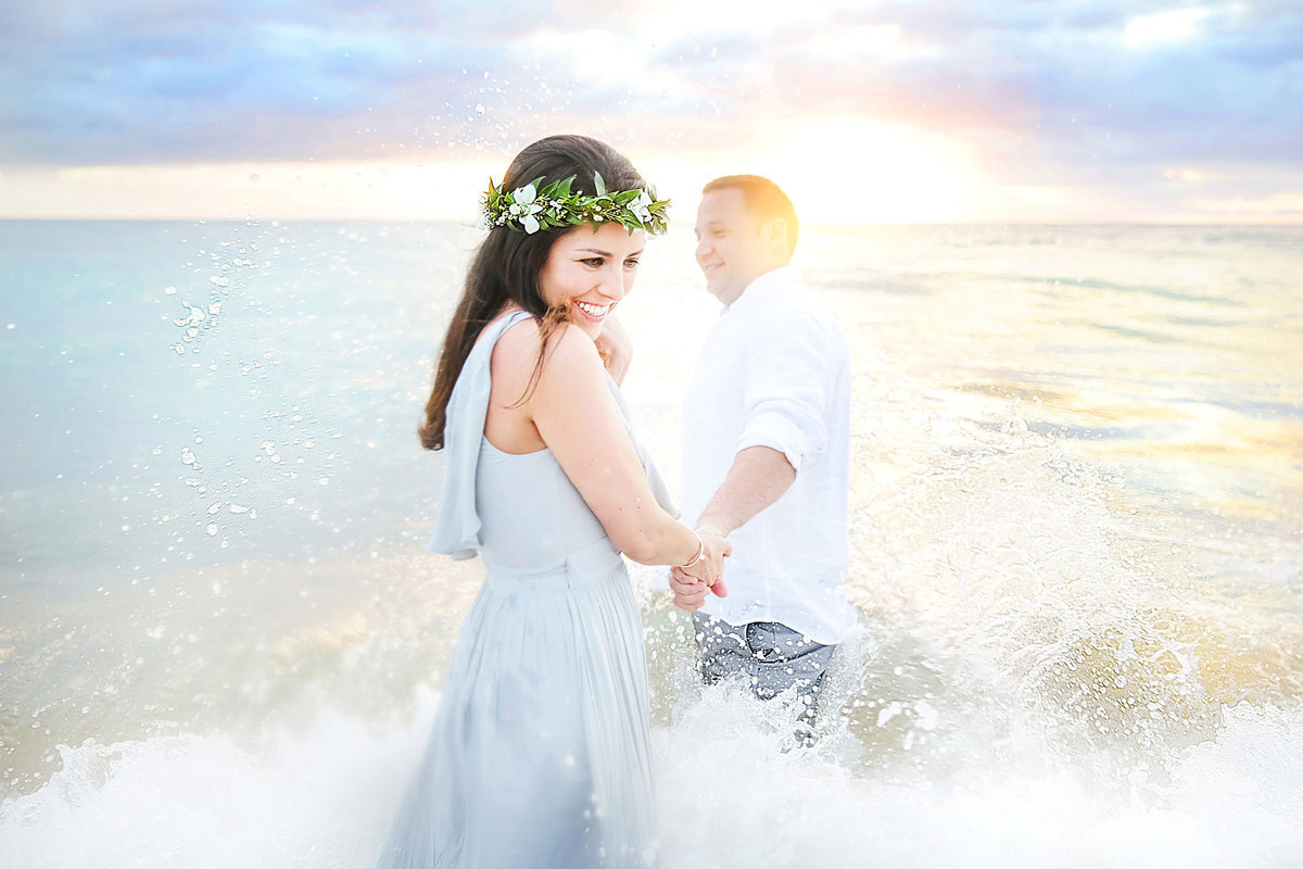 Couple walk in to the water on Maui, wife looks behind her and smiles at the camera as she is photographed by Love + Water
