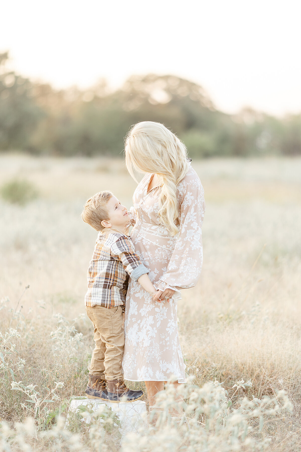 A mother standing in a blooming field with her son as she looks down at him.