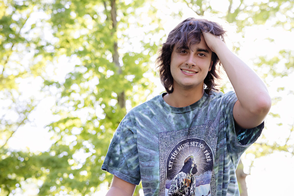 Striking HS Senior male looking down at the camera with his hand in his hair wearing a tie-dye concert t-shirt 