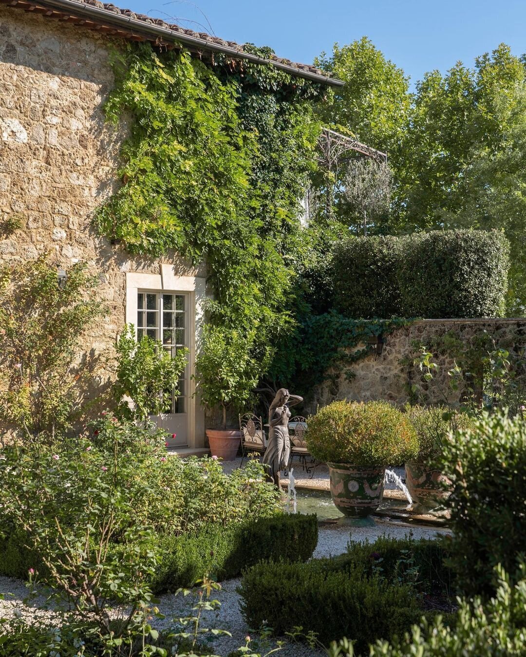 The lush courtyard of Borgo Santo Pietro with ivy climbing along the villa's classic stone exterior and a tranquil pond in the center of the garden