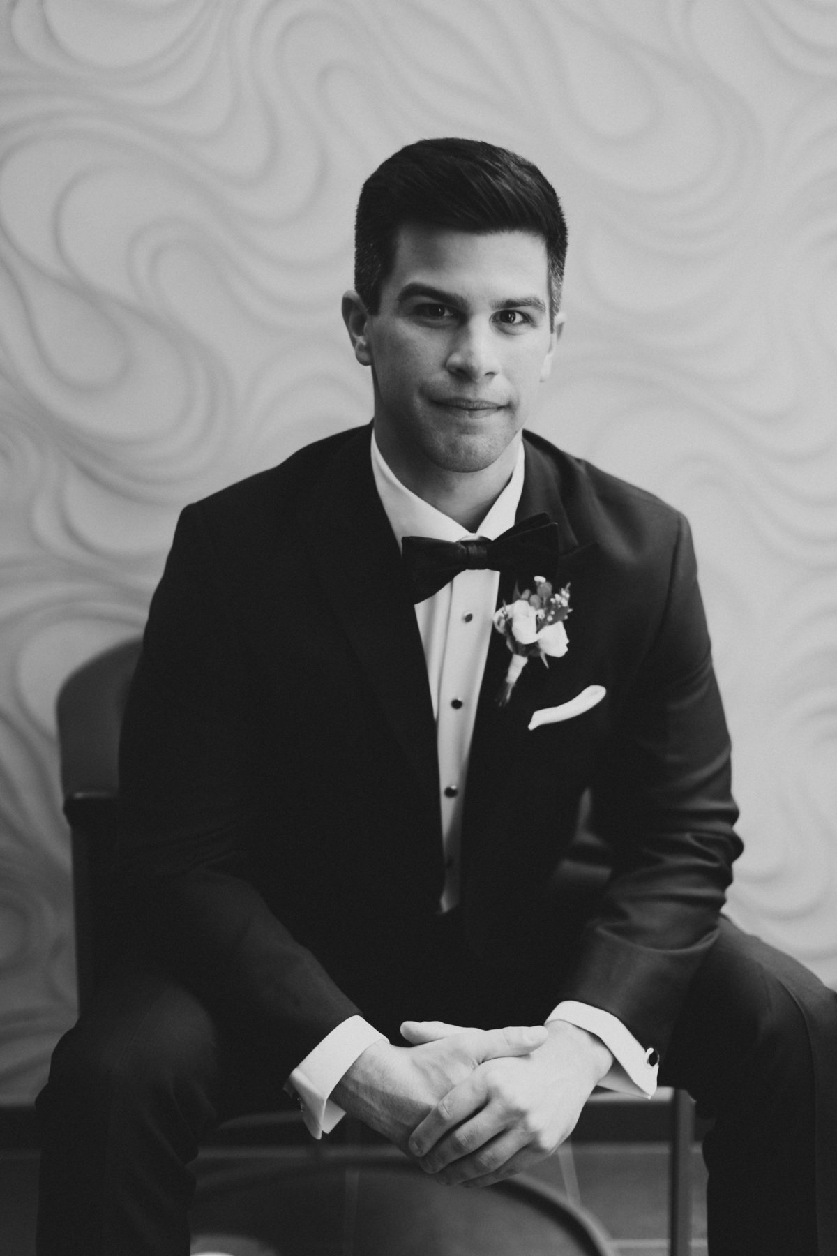 groom sitting on chair in tuxedo during bridal portraits