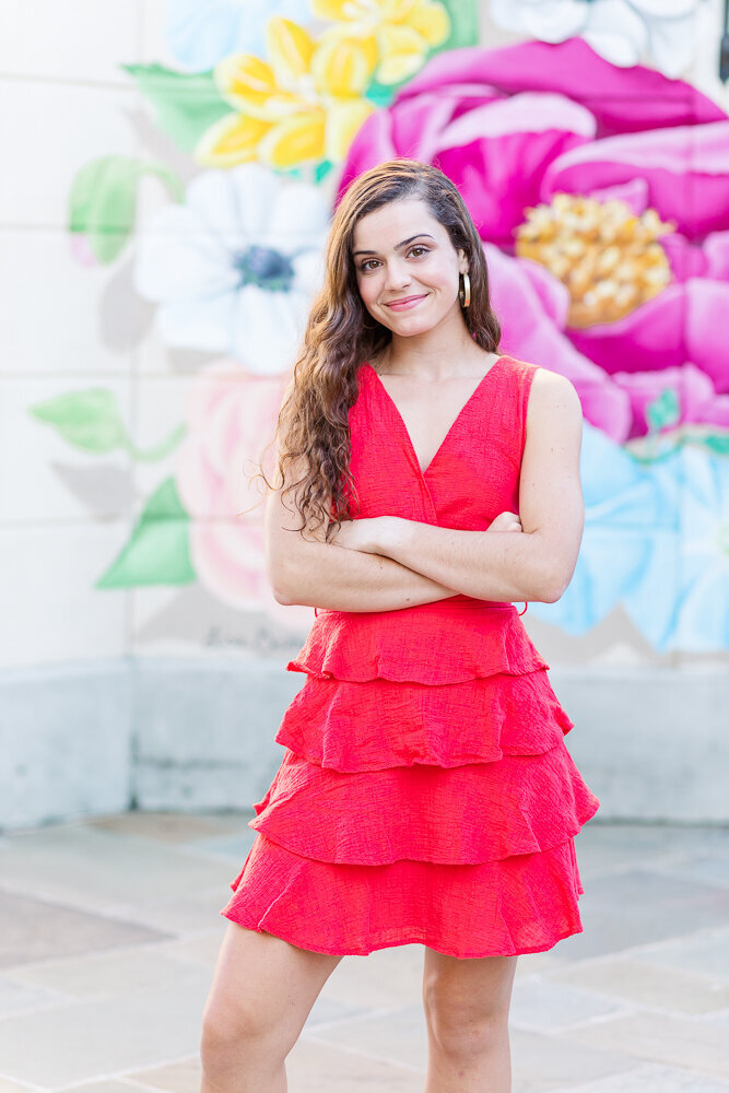 High school senior girl in a red dress standing in front of a beautiful flower mural in Raleigh, NC.