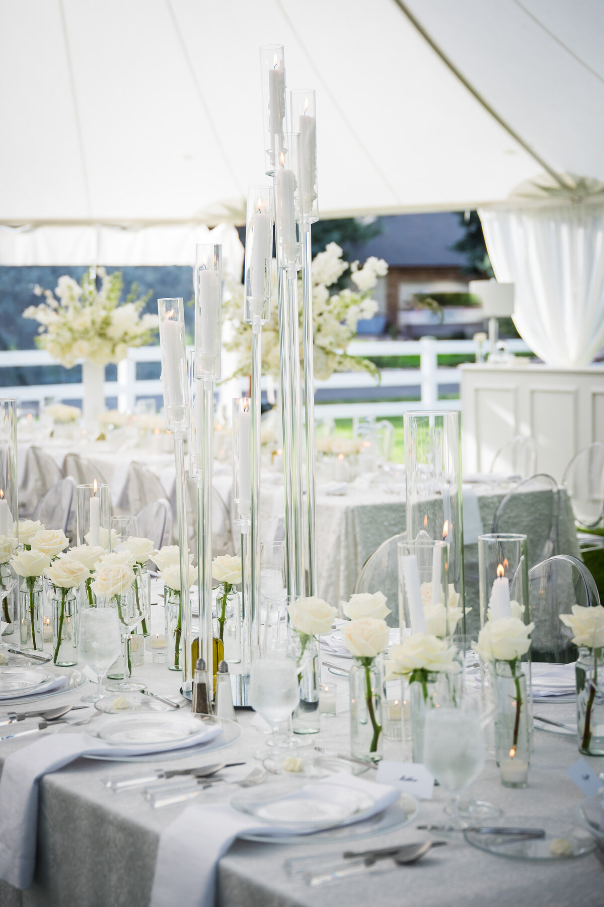 A modern tented reception features an all white table scape with tall candles and white roses.
