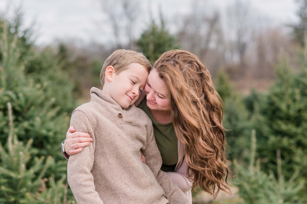 Mom and son nuzzling in close at christmas tree farm