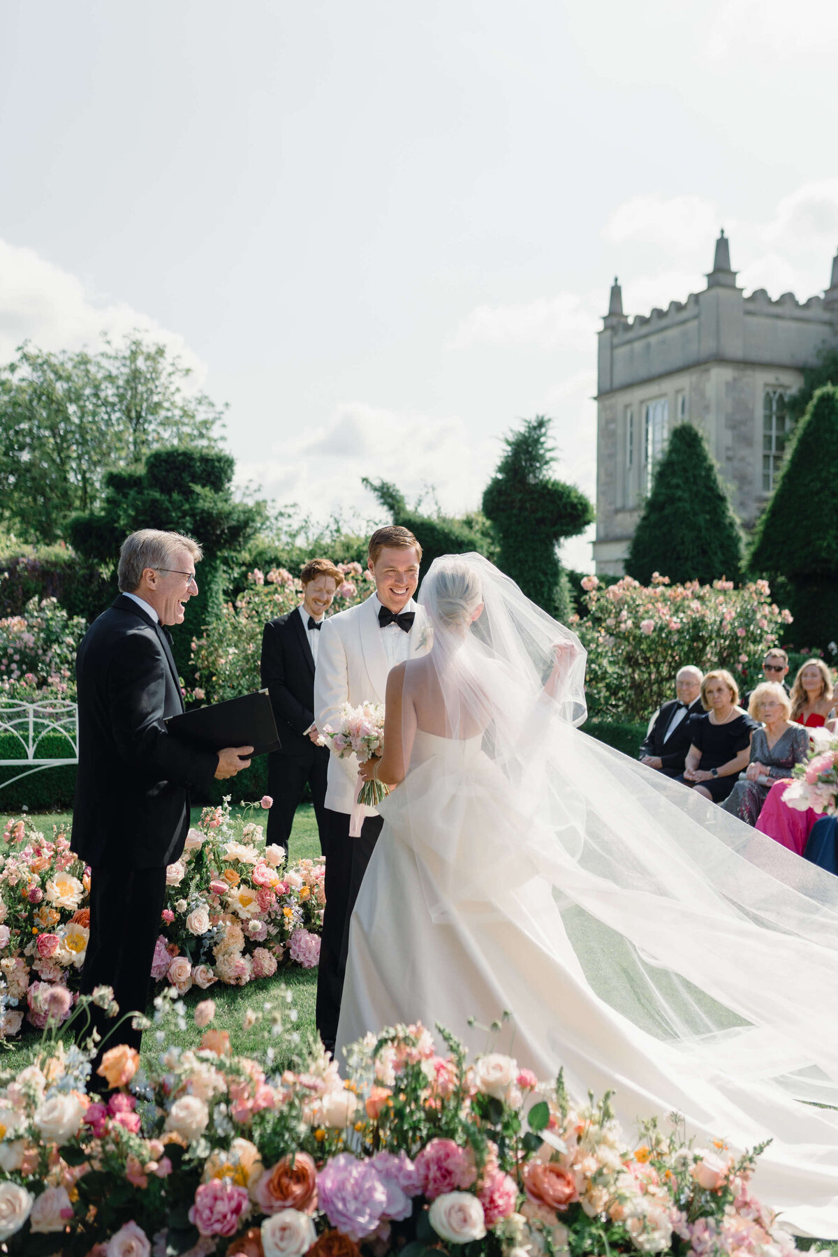 bride and groom take their vows in a garden ceremony amongst a curved wall of pink flowers in the garden of romantic cotswold venue euridge manor