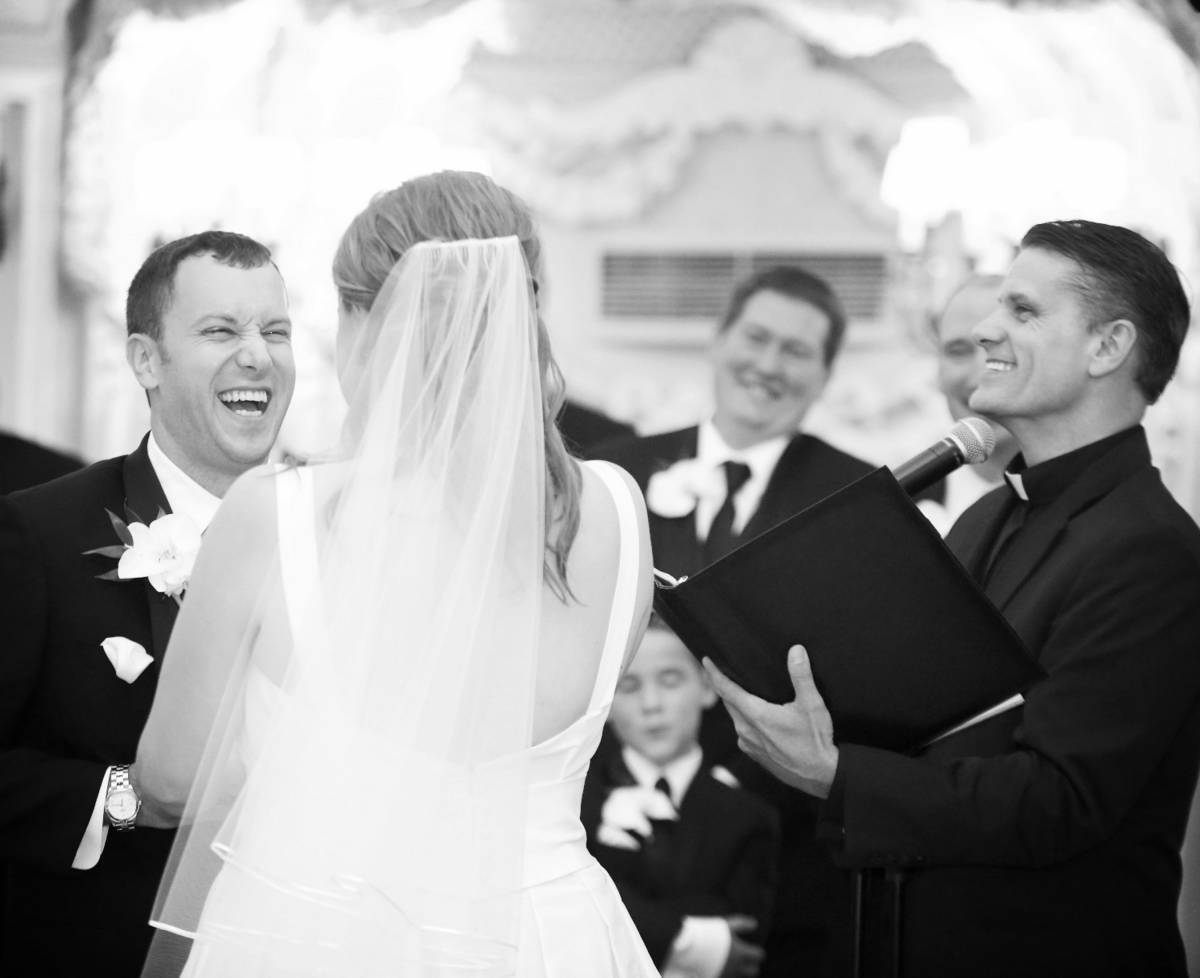 Rev Brad Hughes officiates a wedding ceremony as the groom and wedding party laugh at something said