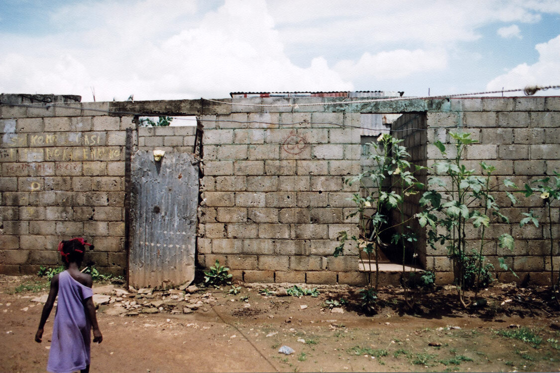A girl in purple dressd stands in front of old cinder block wall that has little holes