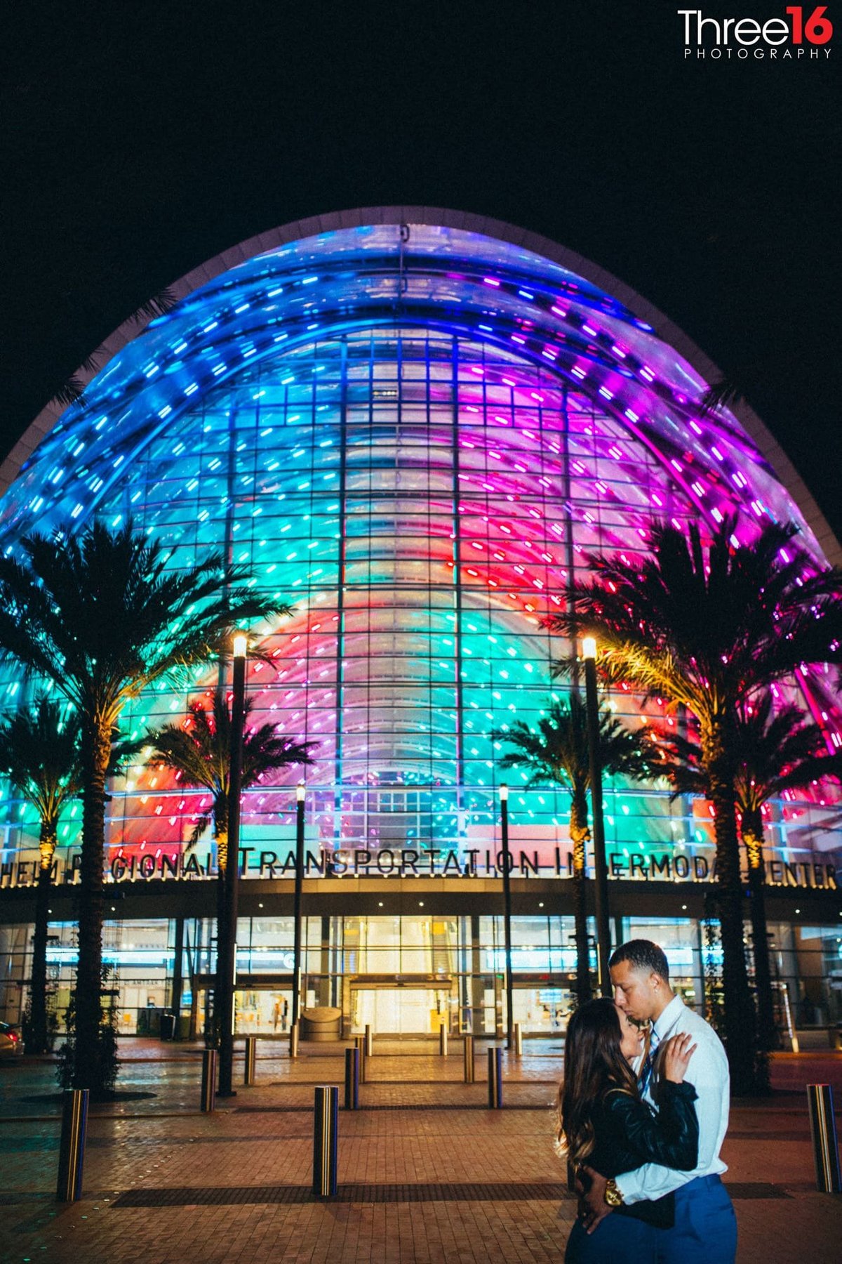 Engaged couple share a kiss in front of the ARTIC Train Station at night in Anaheim