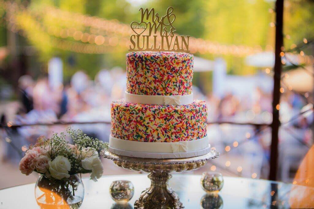 A picture of a two tier wedding cake with rainbow sprinkles on it.