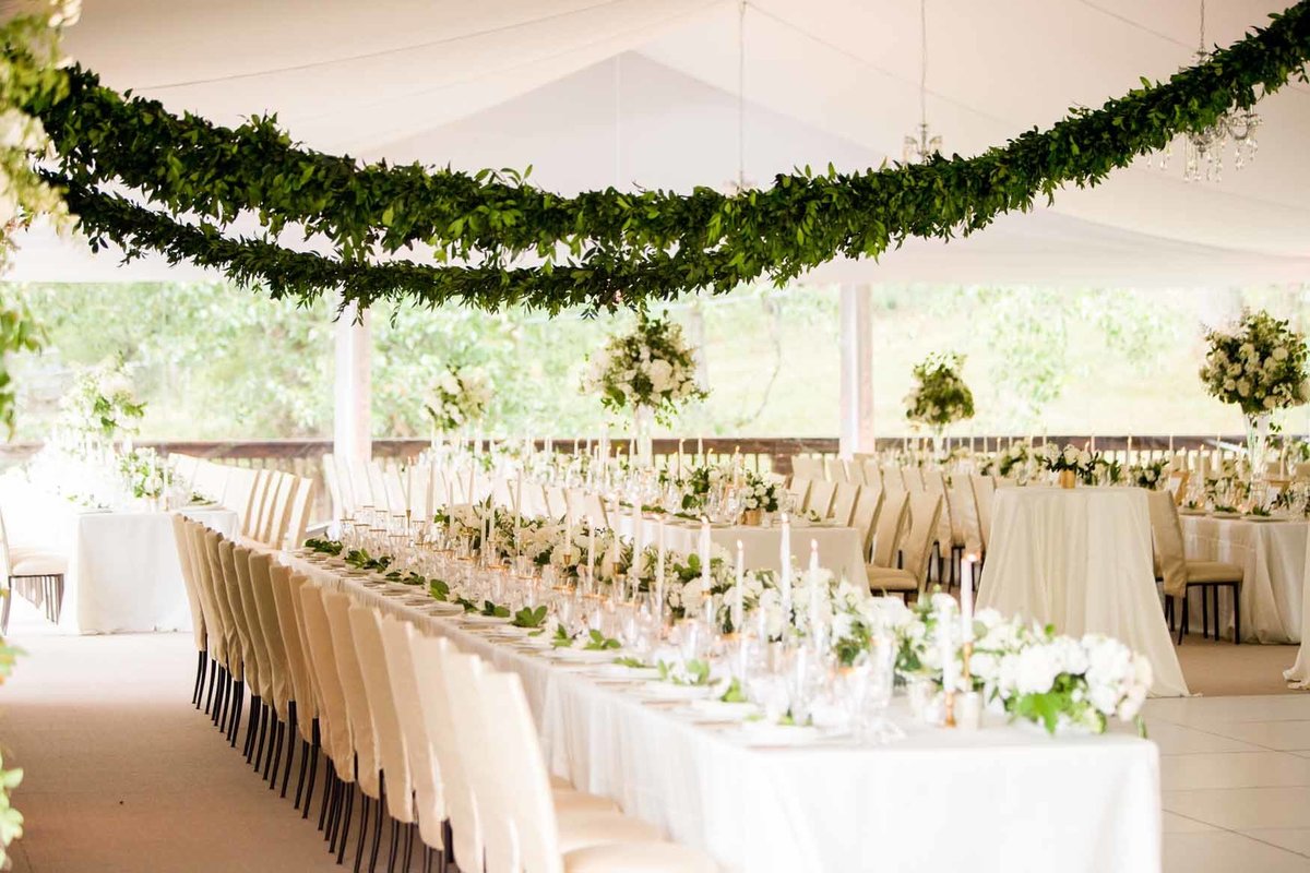 Wedding reception in white tent with long tables and green garlands hanging above
