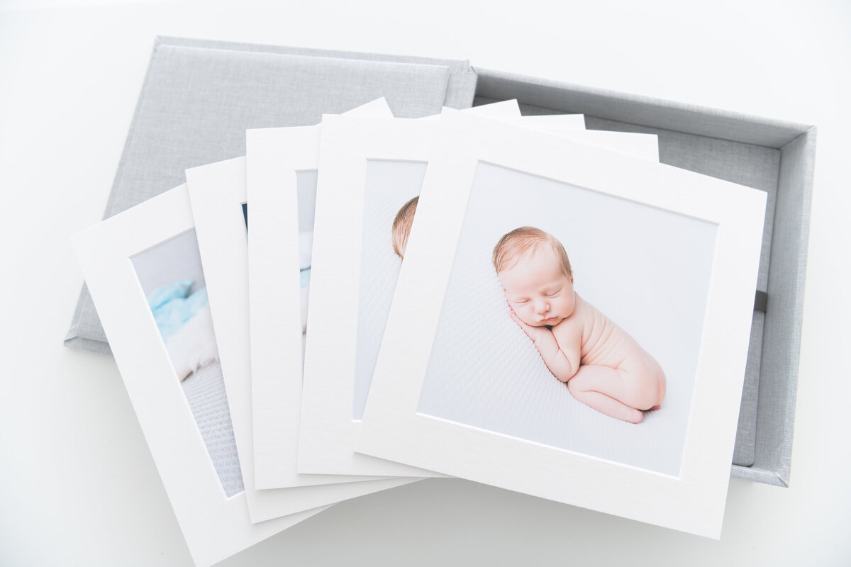 A series of fine art newborn photos lay spread across a fabric box