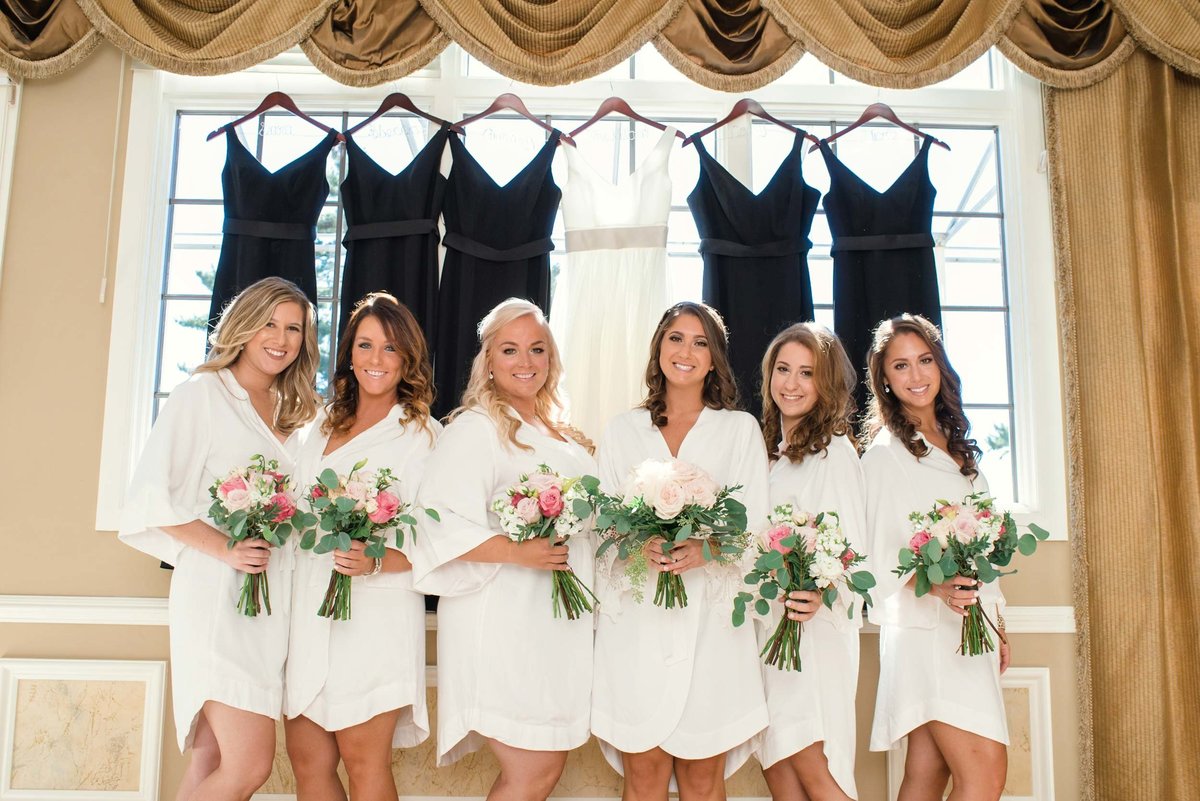 bride and bridesmaids in robes and bouquets in front of hanging dresses at Stonebridge Country Club