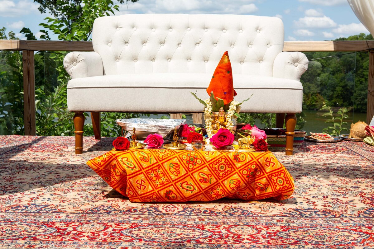 An outdoor seating area with a white couch, adorned with a colorful throw and pillows, overlooking a lake on a sunny day, perfect for park farm winery weddings.