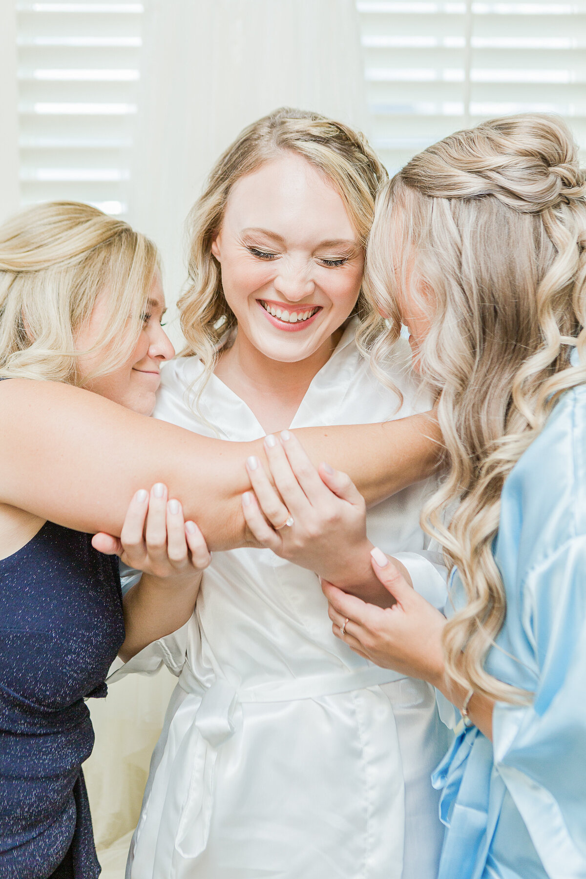 Bride getting ready at the Madison Beach Hotel. Bride is smiling as she is hugged by her mother and sister. Captured by best New England wedding photographer Lia Rose Weddings.