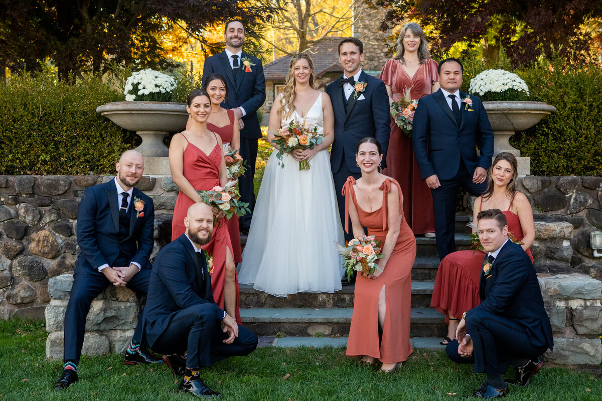 Formal wedding party pose with bride in white dress, bridesmaids in rust orange and men in blue suits Paramount Country club wedding photographer Milestone Images