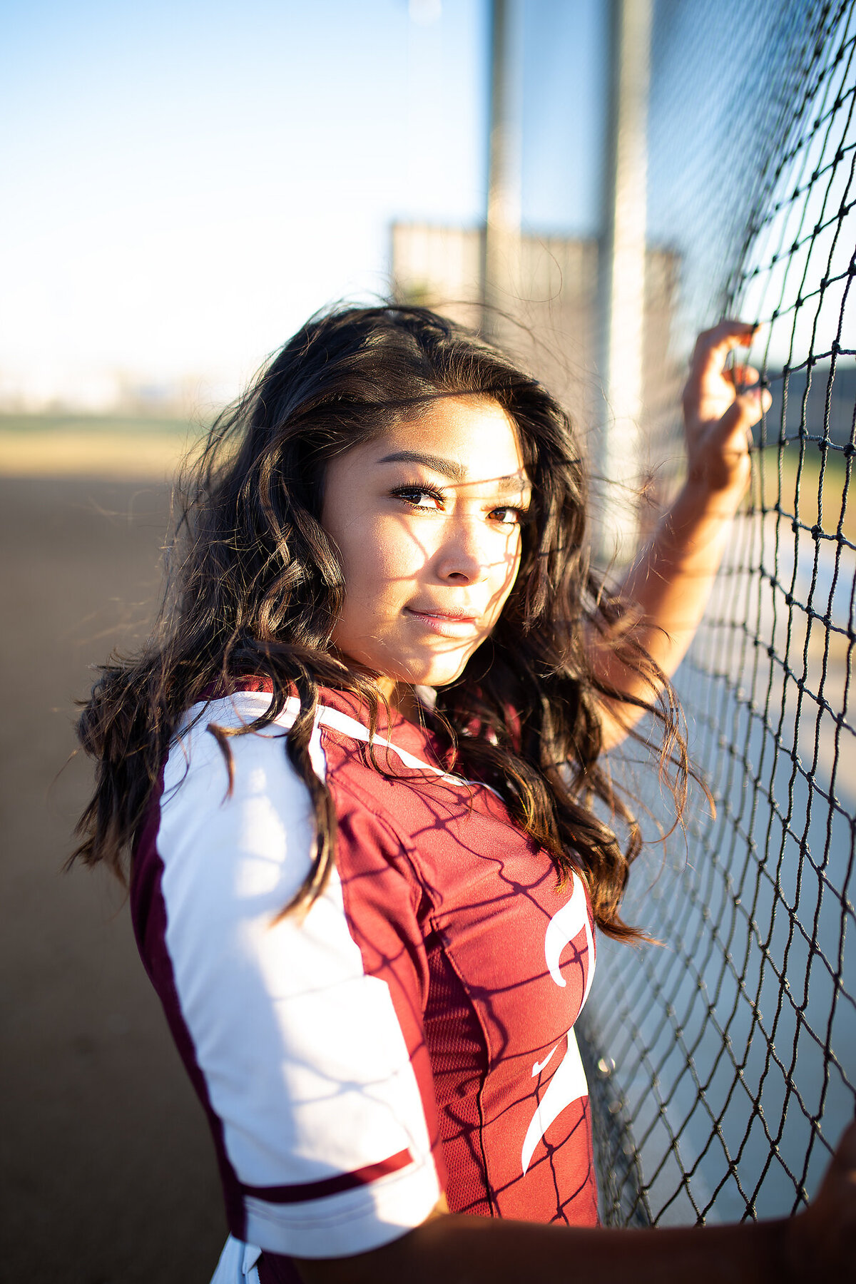 senior girl softball player standing next to field nets
