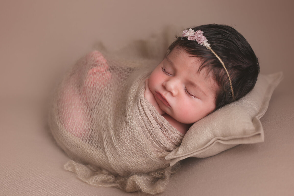 Newborn baby sleeping wrapped  up on her back on a pillow on a beige background.