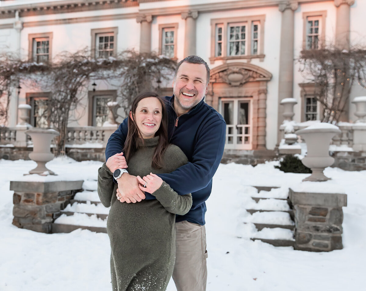 A couple laugh together during an embrace for their maternity session at Liriodendron Mansion in Bel Air, MD.