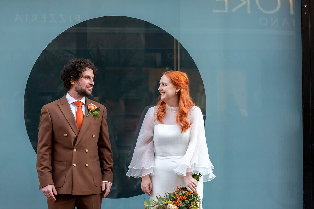Red head bride standing infront of Green Exmouth market shop window with groom