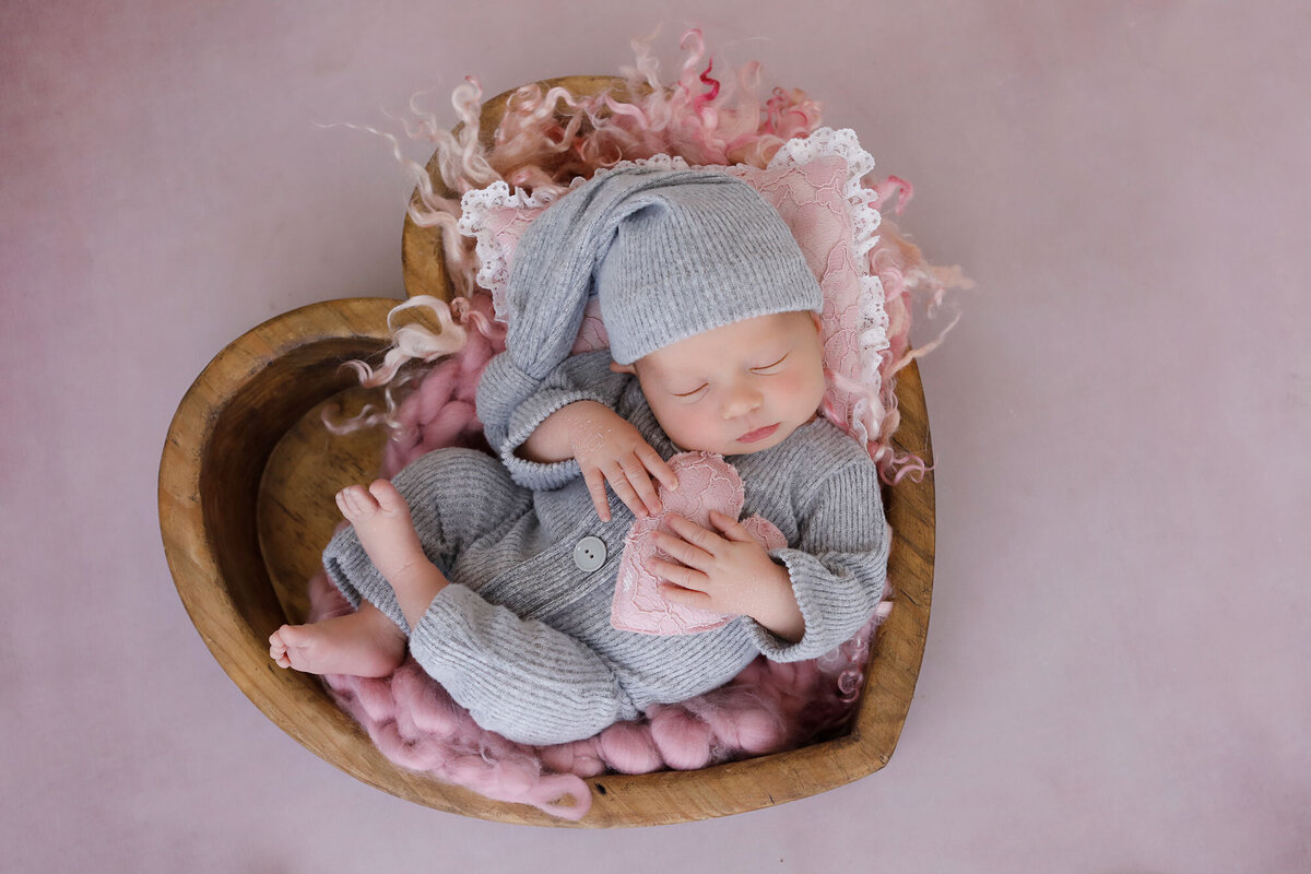newborn-baby-girl-dressed-in-grey-sleeping-in-a-wooden-heart-bowl