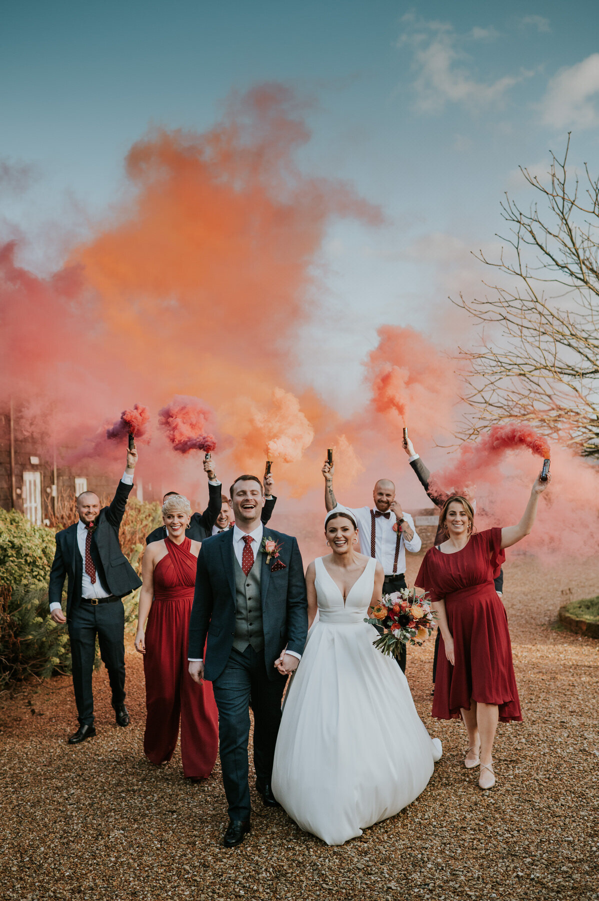 A bride and grrom with their bridal party walking with smoke bombs