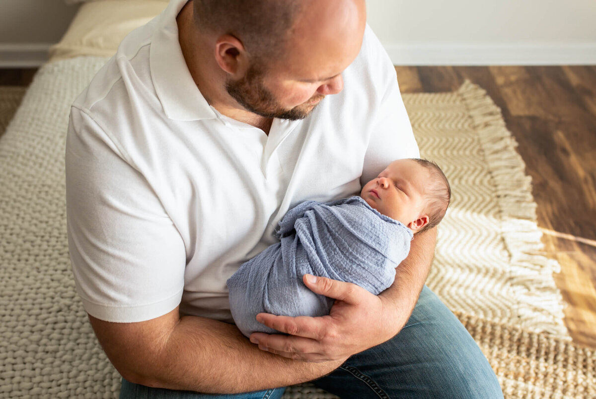 A new daddy holds his newborn baby boy who is wrapped in a blue blanket