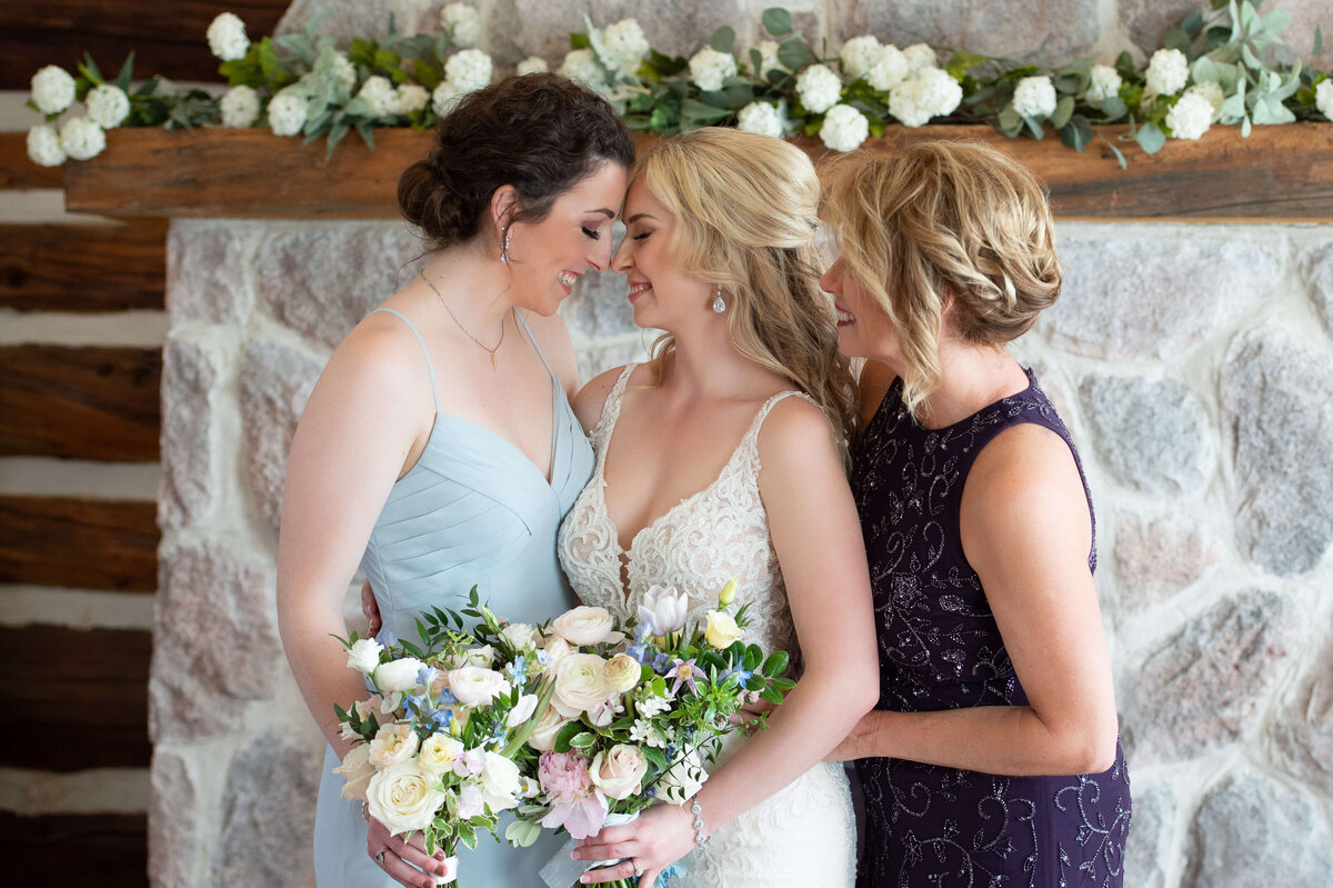A bride hugs with her mom and sister for her Ottawa wedding photography at Stonefields Estate