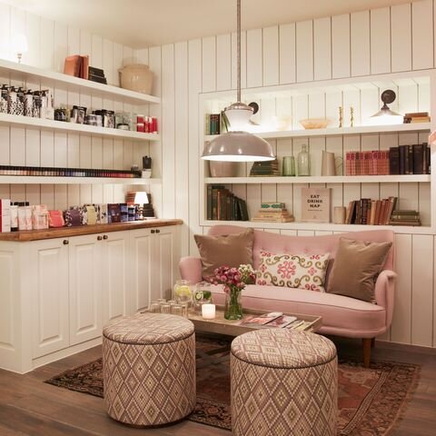 Lounge area with white wood board walls and built in shelving millwork, pink vintage sofa, ottomans upholstered with geometric fabric on top of vintage rug