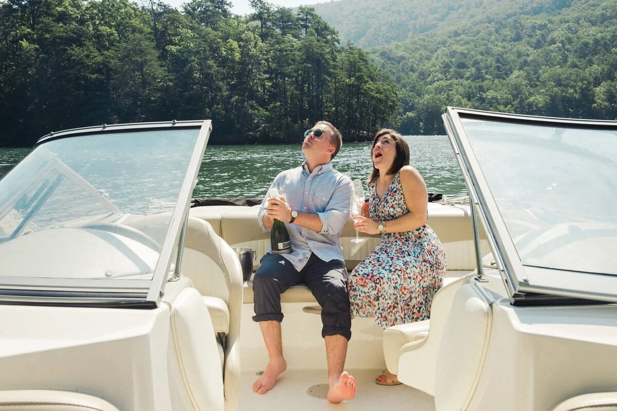 A couple enjoying a sunny boat ride, with the woman laughing heartily and the man holding a bottle