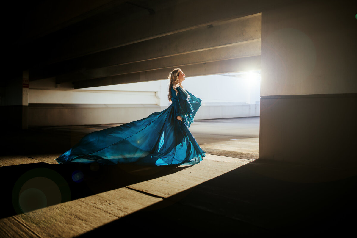 amazing harsh loight maternirty photos taken in a parking garage with a flowy blue maternity gown with backlight and dramatic lighting