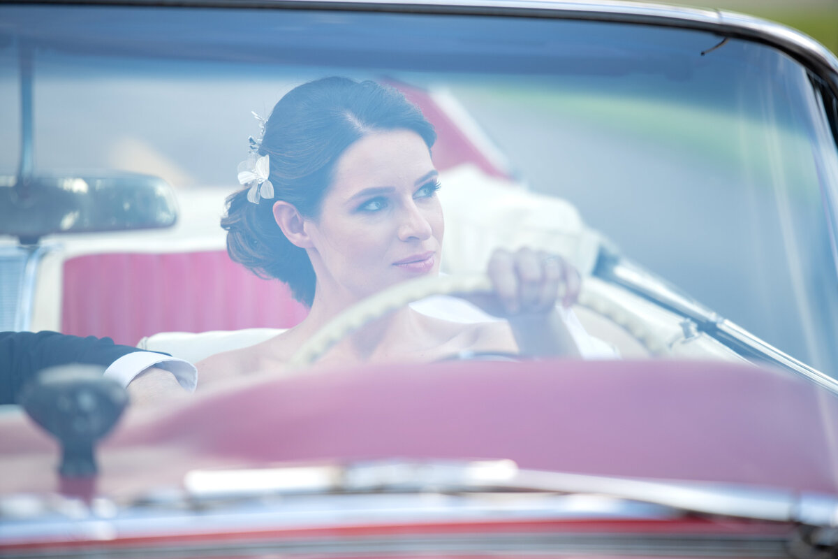bride is taking groom on a  ride with vintage convertible car