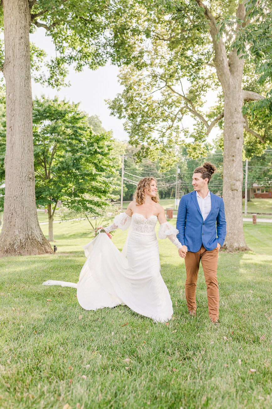 bride and groom walking and holding hands at mustard seed hill taken by louisville wedding photographer brittani riggs photography