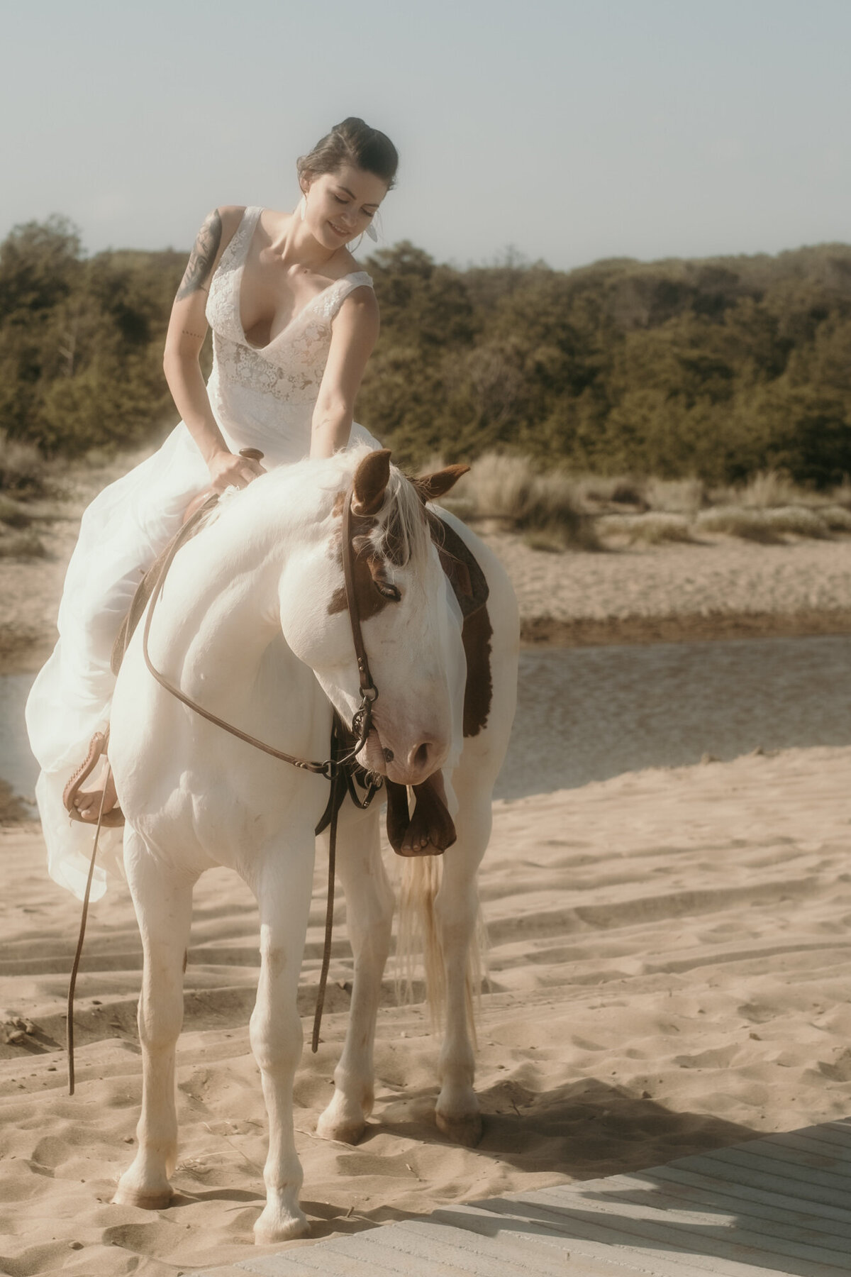 Die Braut sitzt auf einem weißen Pferd mit braunen Flecken. Sie streichelt es am Hals.