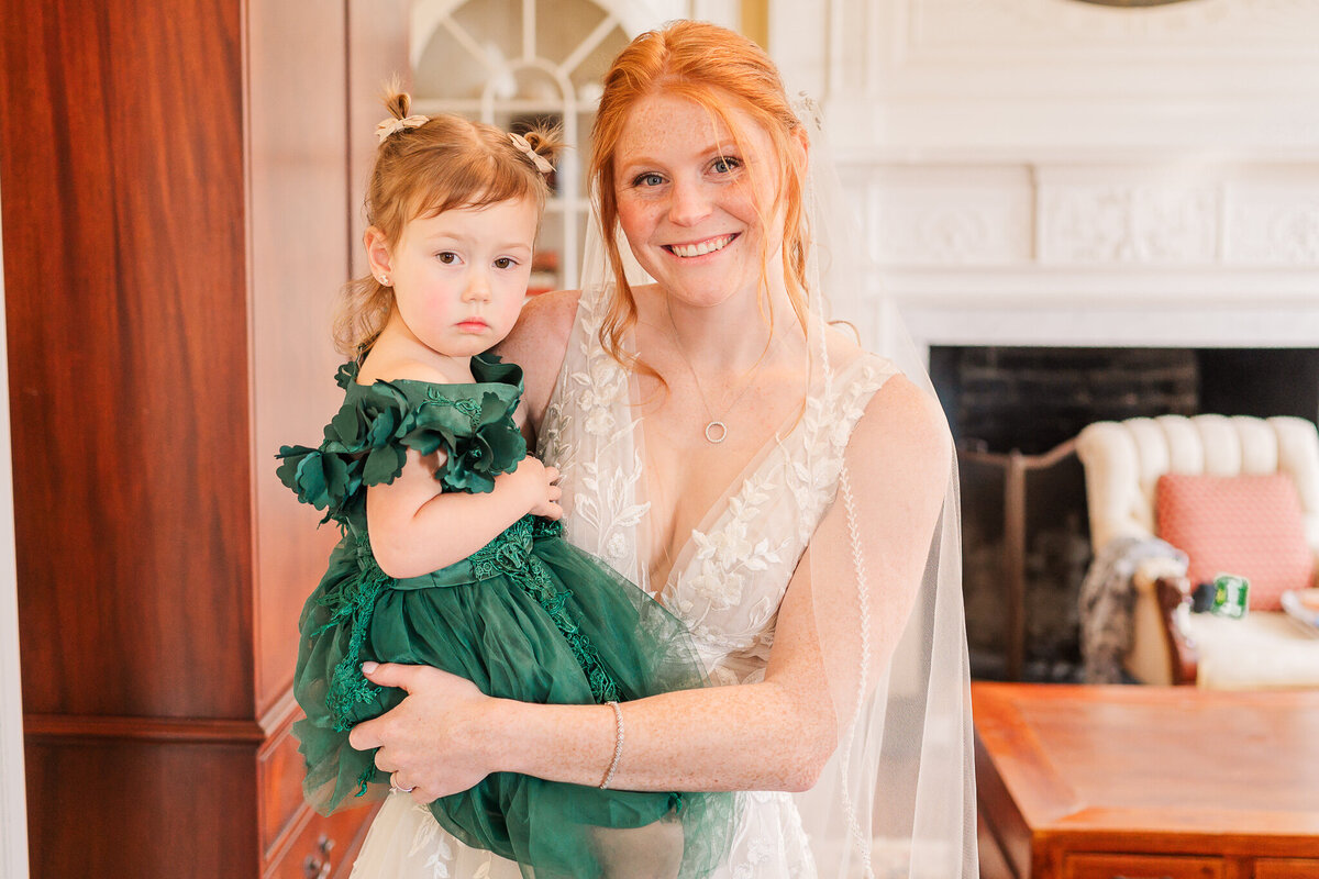 A bride holding her flower girl on her wedding day by JoLynn Photography, a North Carolina wedding photographer