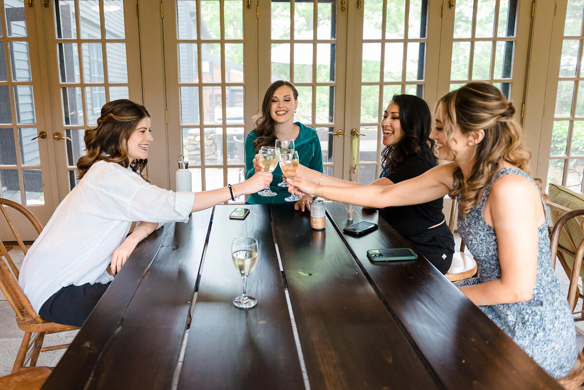 A group of four women toasting with glasses of white wine at a wooden table.