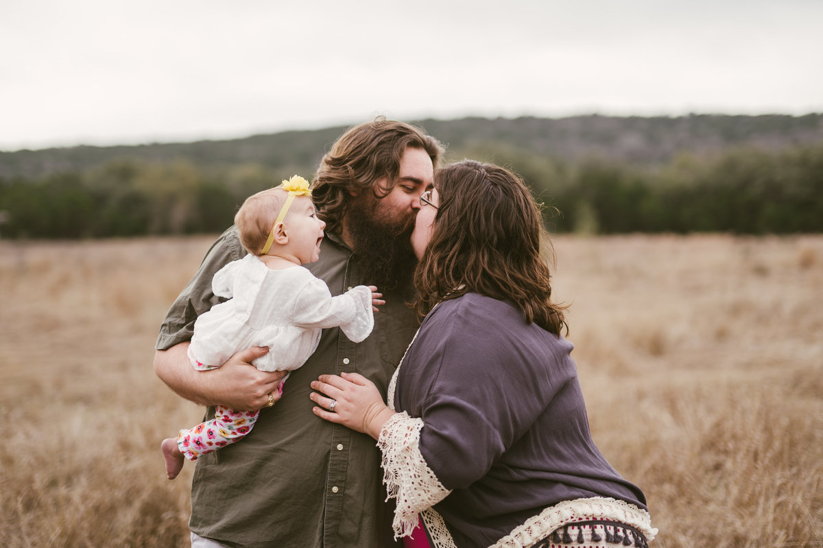 family portrait session mom and dad kissing and dad holding baby by San Antonio photographer