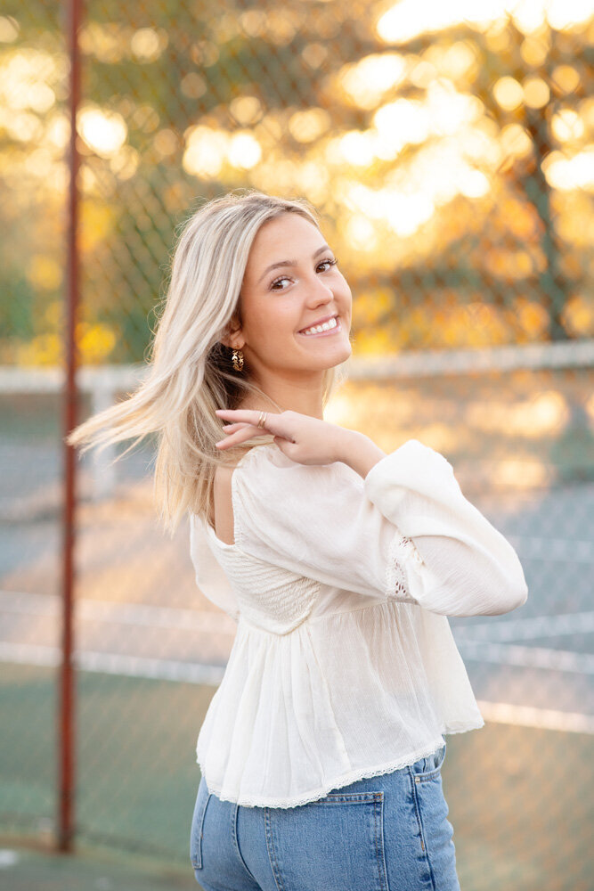 Senior session of young woman in white top against fence