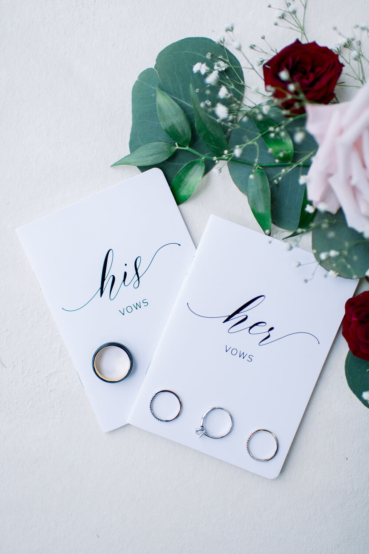 his and her vow books with wedding rings and florals by arkansas wedding photogapher