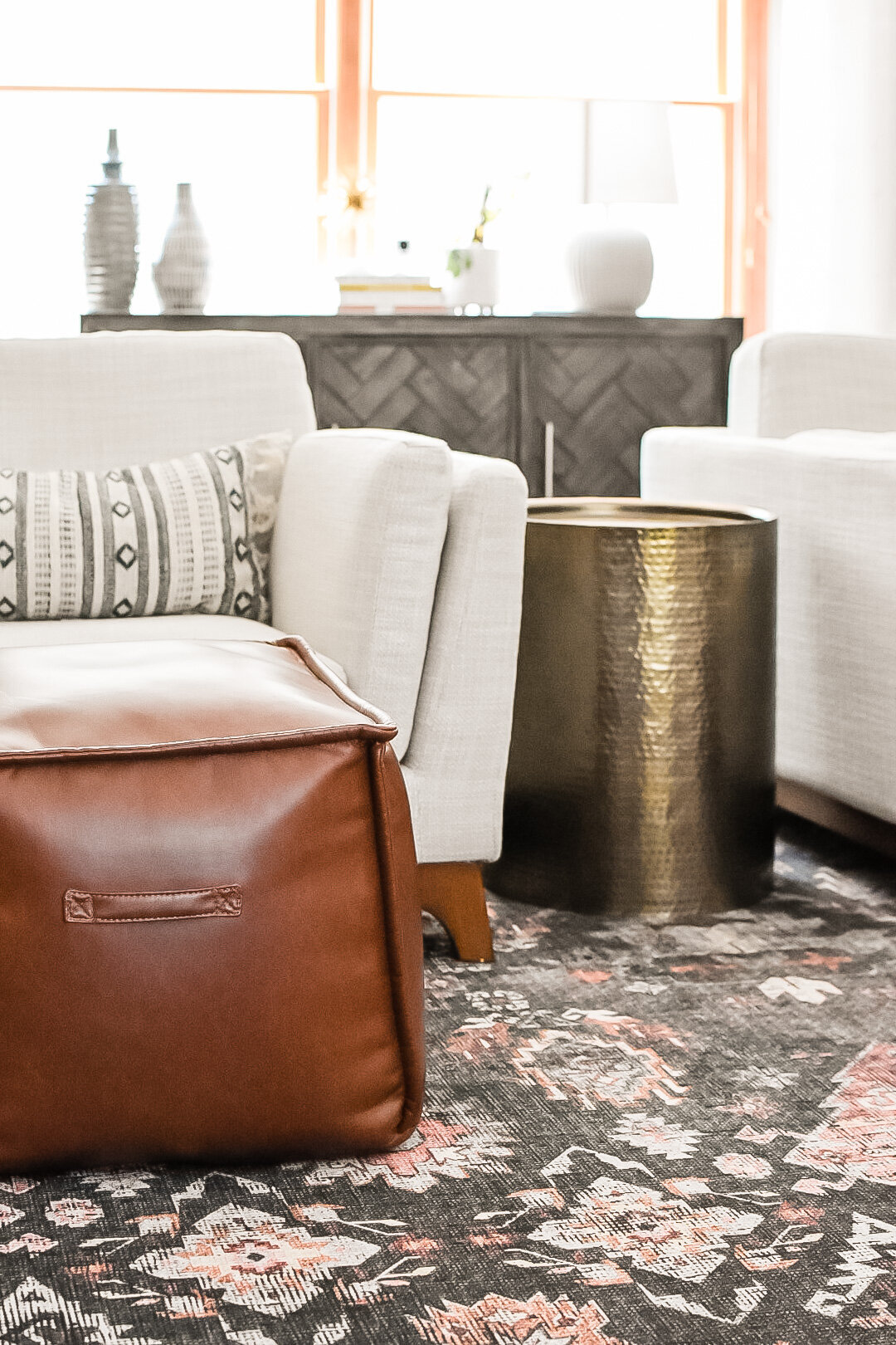 A brown leather ottoman sits on a blue patterned rug