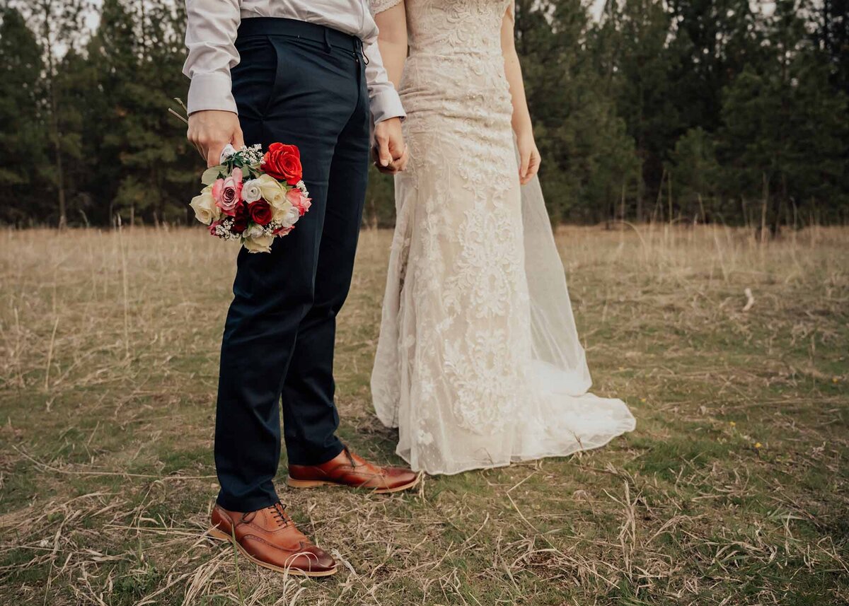 Maddie Rae Photography bride and groom standing side by side holding hands. he is holding her flowers. this is shot from a low angle with no faces in the picture
