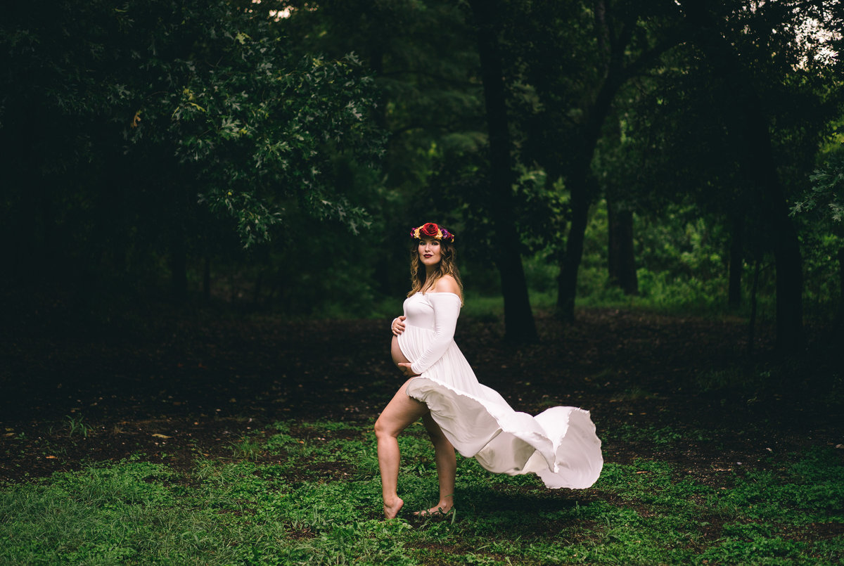 Maternity session of woman wearing flower crown and white flowing dress at Denman Estate Park in San Antonio.