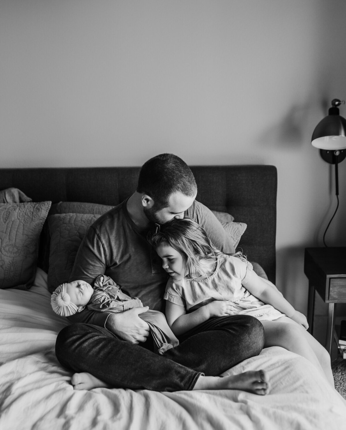 Newborn Photographer, Dad snuggling with older daughter and baby daughter on the bed.